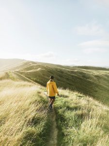 A man in a yellow jacket hikes along a grassy hill during a bright sunny day, capturing adventure and nature.